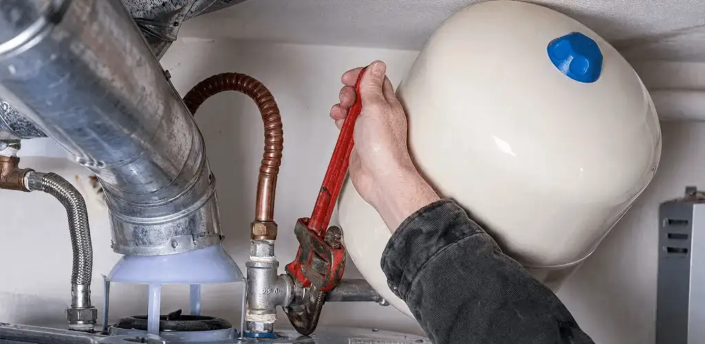 Water heater repair technician tightening plumbing connections near a tank unit in Overland Park, KS